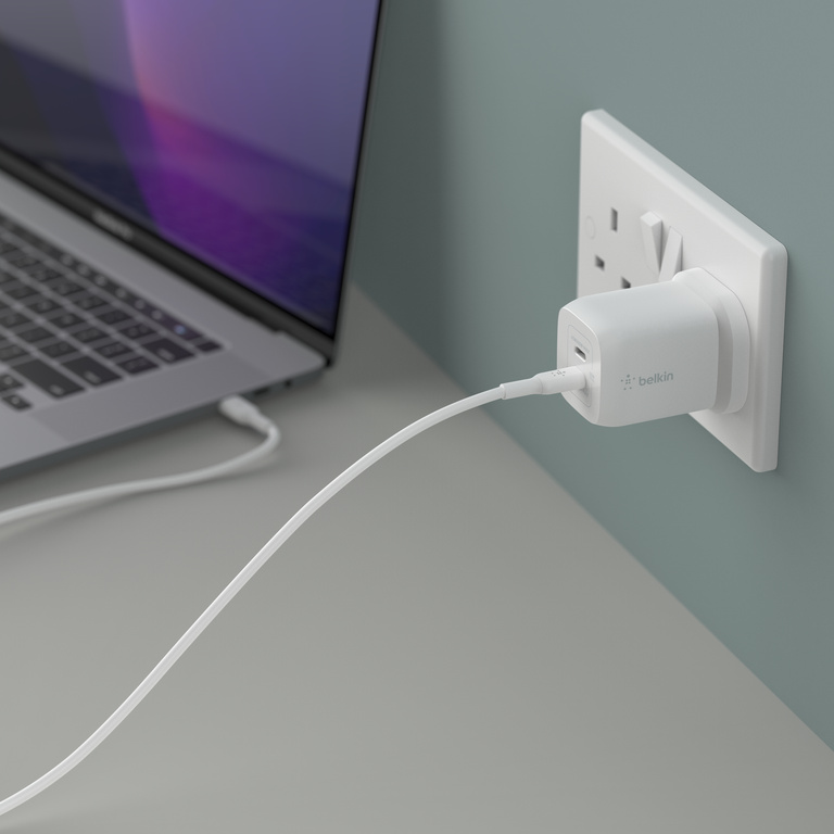 An image of a Belkin Dual USB-C® GaN Wall Charger with PPS 65W in use, plugged into a wall outlet with USB-C cable plugged into bottom port. 